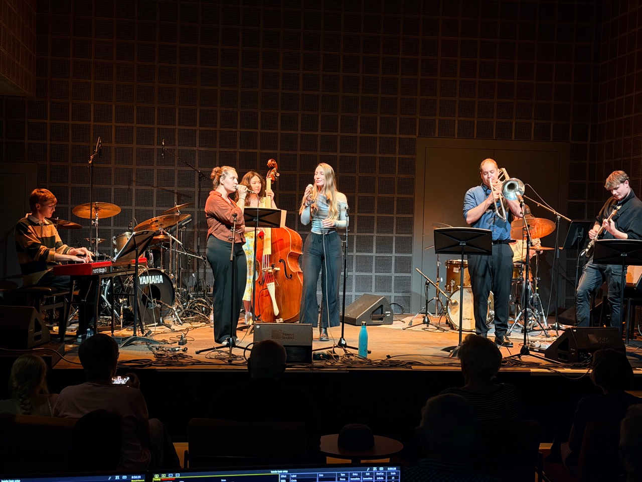 Xiao playing double bass behind two vocalists, with keyboard, drums, trombone and guitar on stage