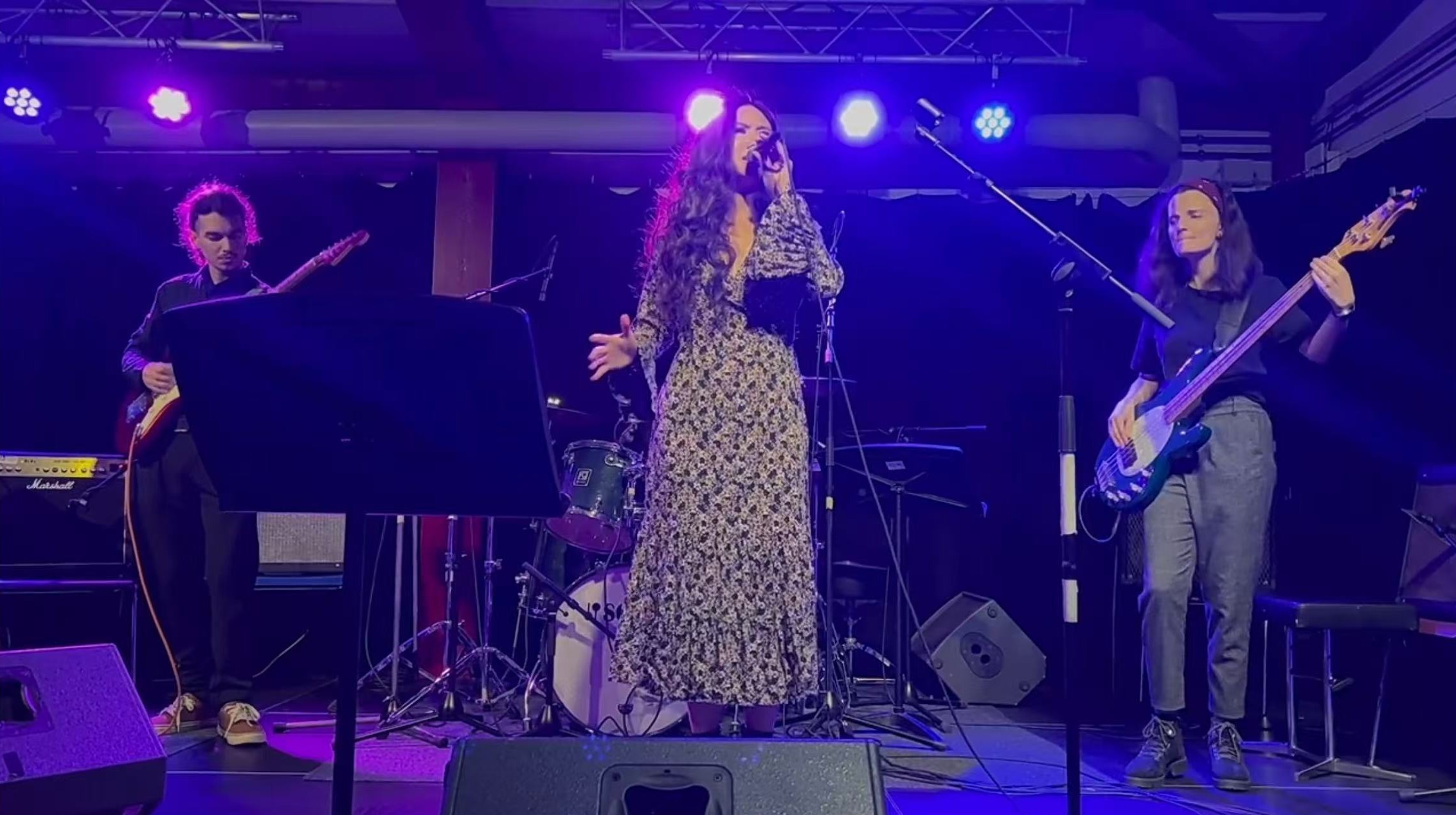 Xiao singing with a guitarist and bass guitarist at WIAM under purple stage lights